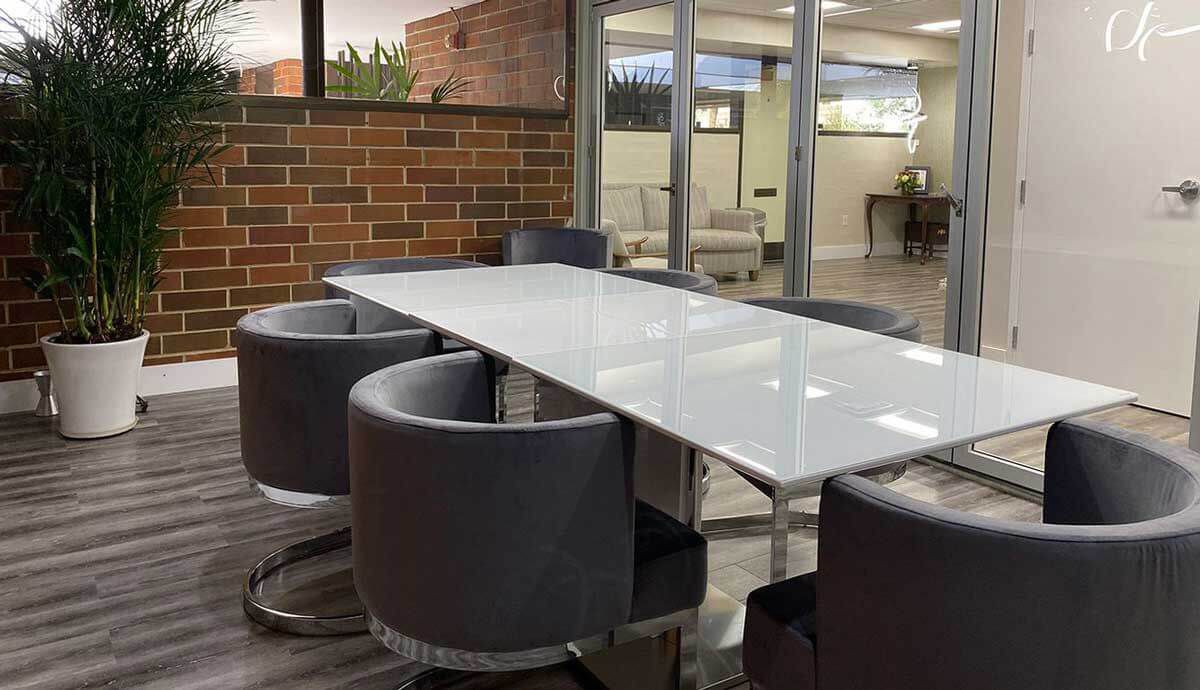 The image shows a modern office space with a large glass table surrounded by circular chairs, set against a brick wall and featuring a sleek design with contemporary furniture and decorative elements.