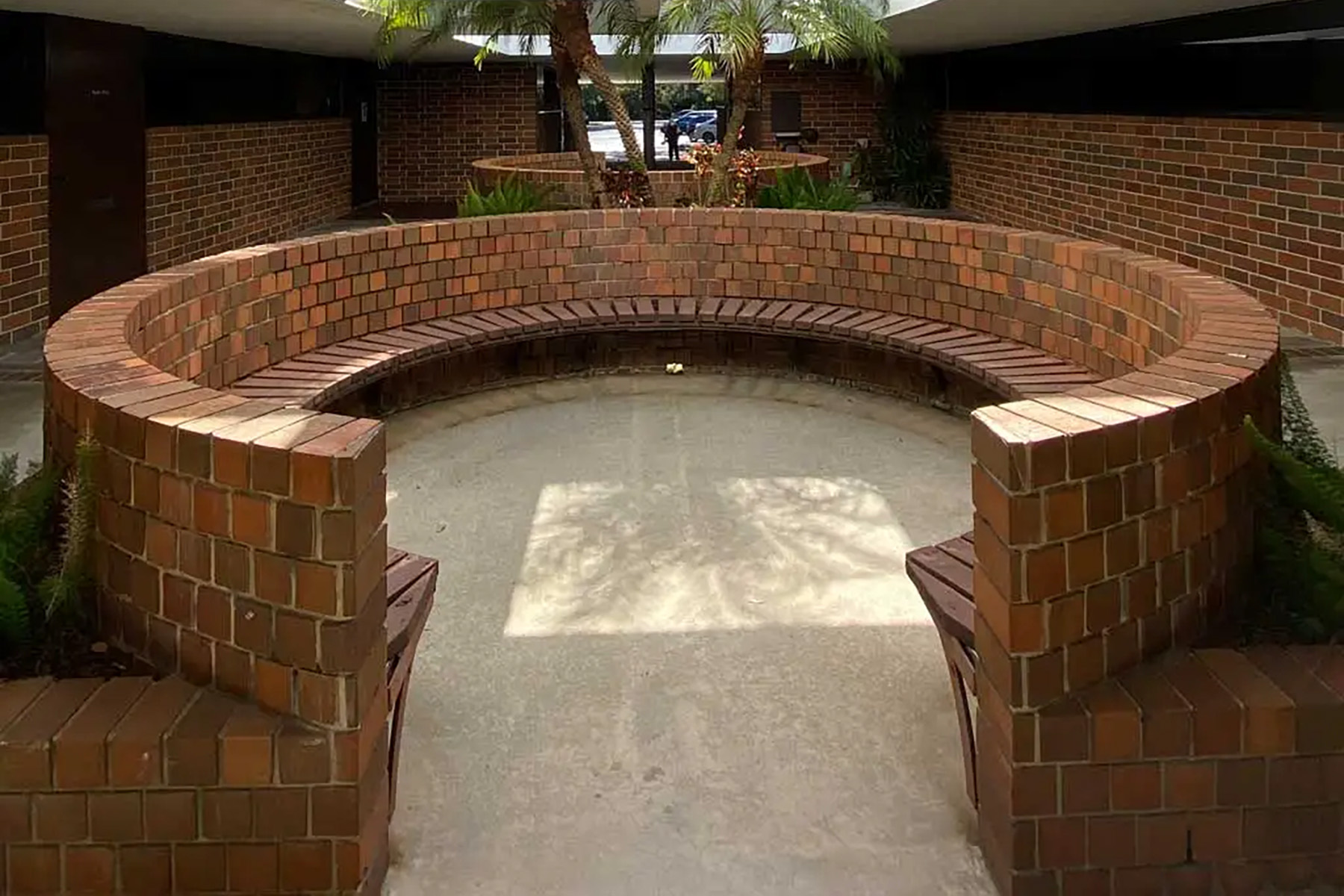 The image shows a brick bench with a curved seating area, situated within an outdoor courtyard space.