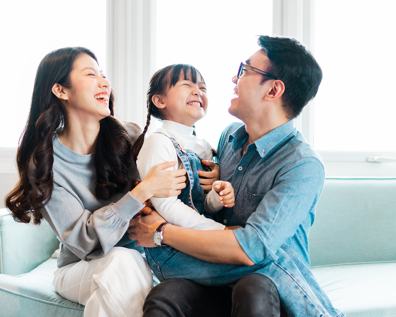 The image shows a family moment with a man, woman, and child smiling and embracing each other on a couch.