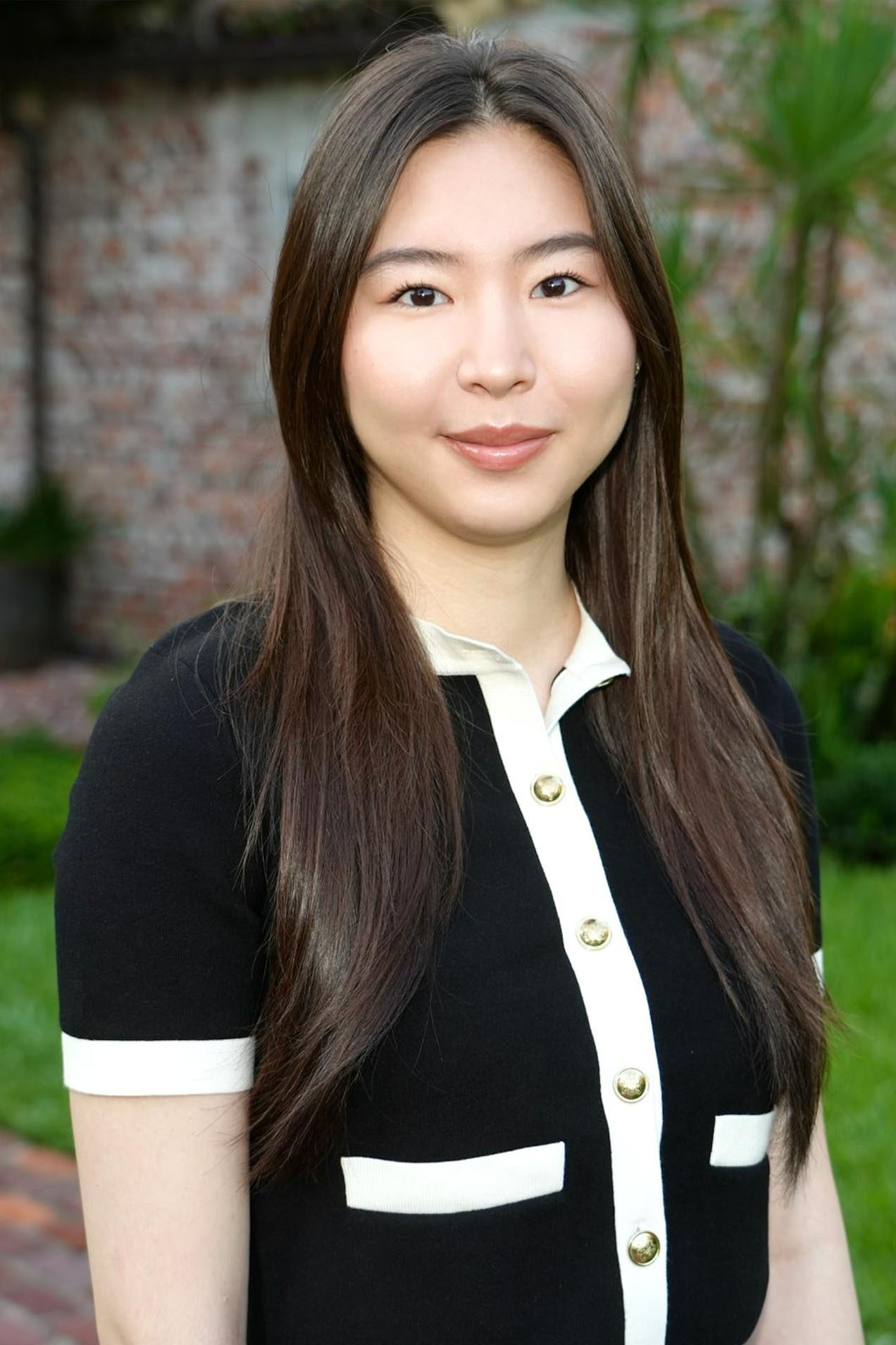 This is a color photograph featuring a woman with long dark hair, wearing a black and white striped blazer over a black top, posing for the camera with a neutral expression.