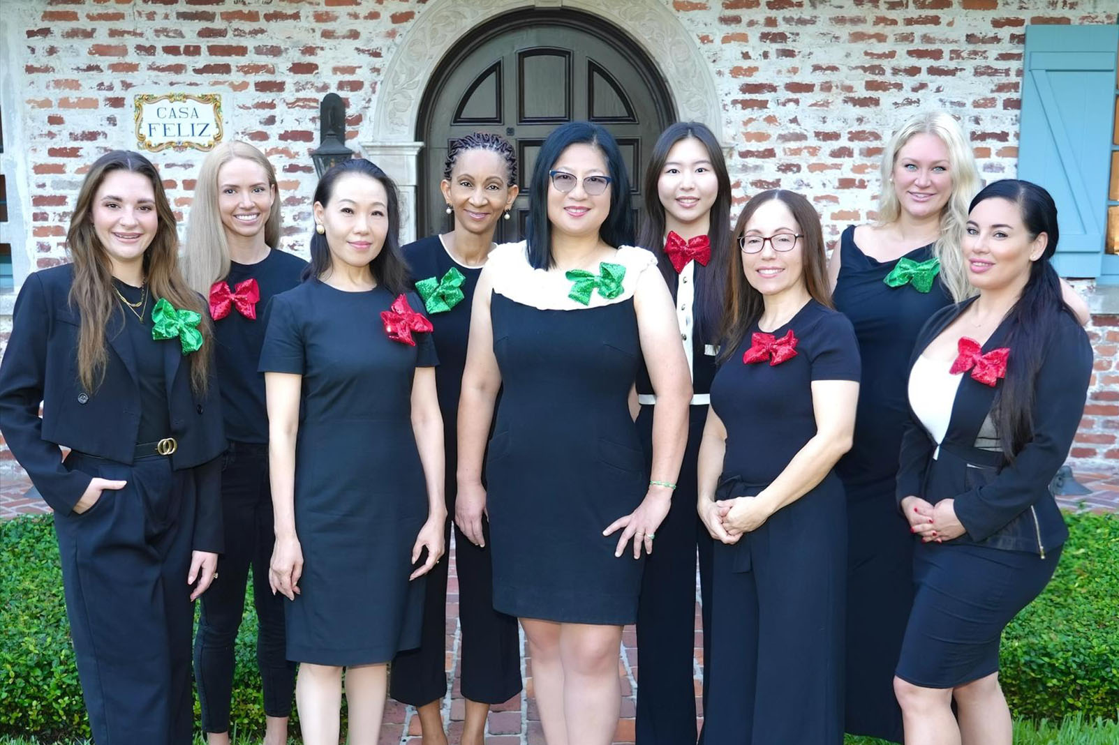 The image shows a group of individuals, likely a choir, dressed in black formal attire, posing outdoors in front of a building with a brick exterior and a staircase leading up to it.