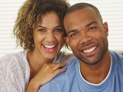 A man and woman smiling at the camera, posing together with warmth and happiness.